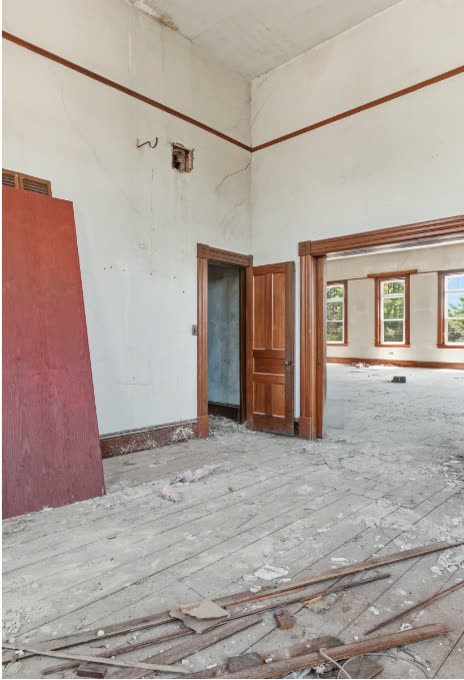 The third floor today: bare plaster, debris across wide plank floors, tall windows lighting an empty shell