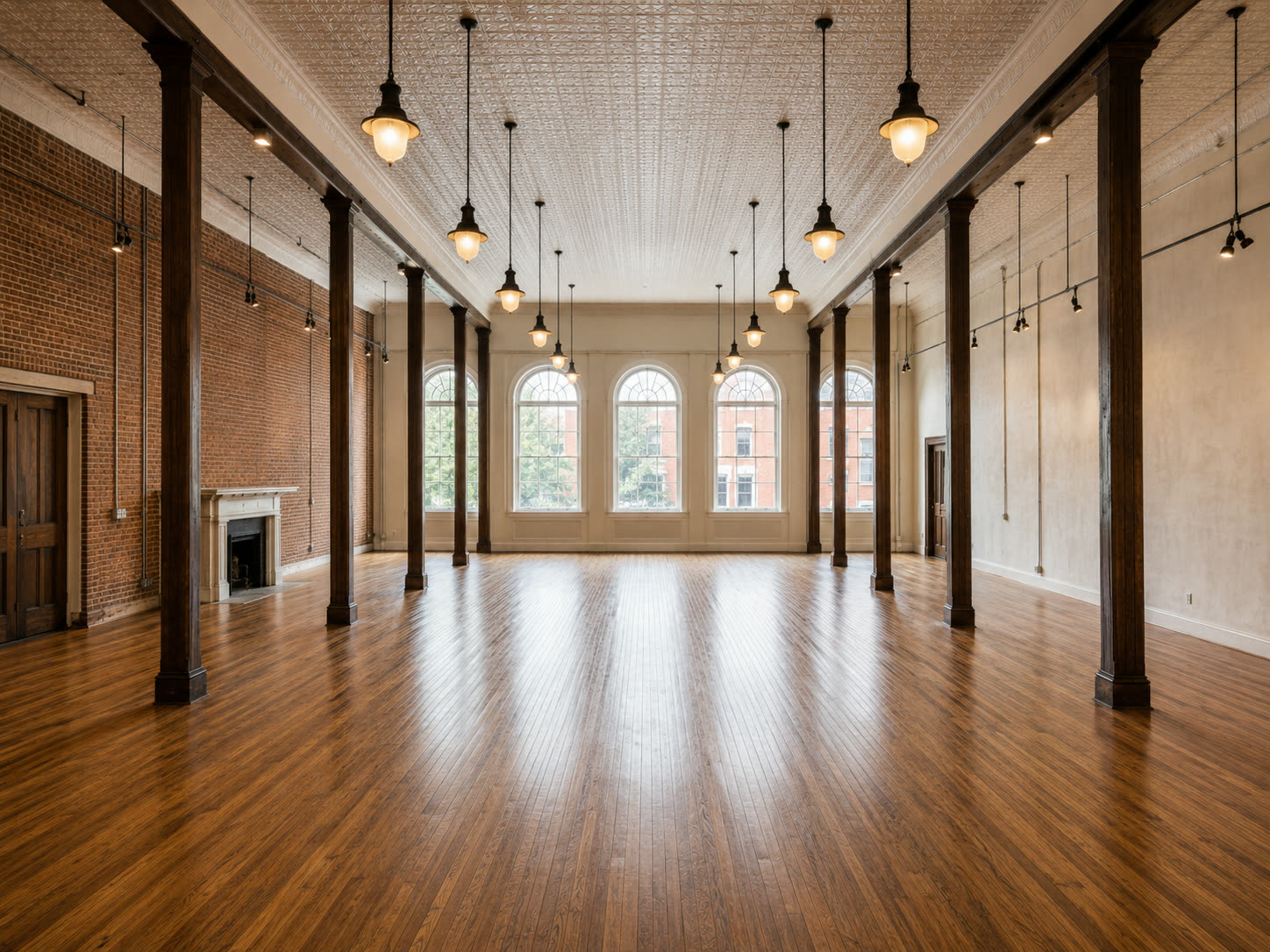 A vast restored hall with dark wood columns, pressed tin ceiling, pendant lights, arched windows and empty polished floors