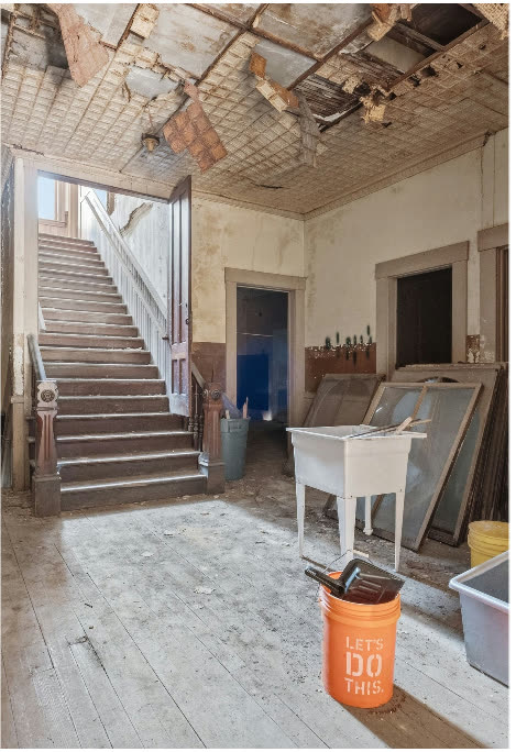 The staircase today: collapsed tin ceiling panels hanging, debris on the floor, an orange bucket printed LET'S DO THIS